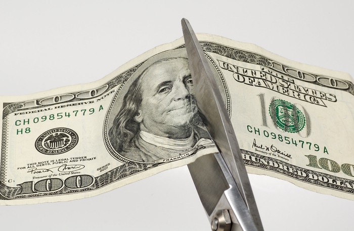 Scissors cutting a one hundred dollar bill in half.