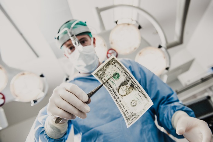 A surgeon holding a one dollar bill with surgical forceps.