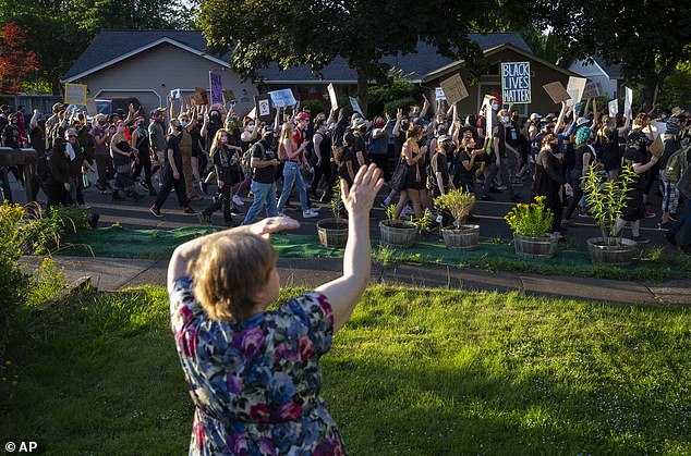 Rita Castillo waves to Black Lives Matter marchers as they pass her home in Springfield, Oregon, on Friday, June 27