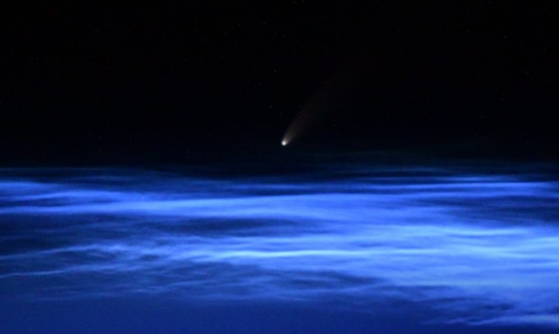 Small glowing dot with barely visible tail over brilliant blue, wavy, horizontal streaks of clouds.