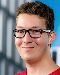 Smiling young man with eyeglasses and buildings in background.