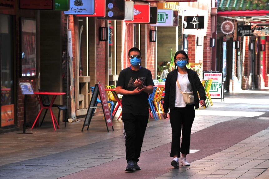 Two people wearing blue face masks walk through an empty walkway in Chinatown 
