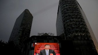A large public video screen shows Xi Jinping in front of a dark cityscape.