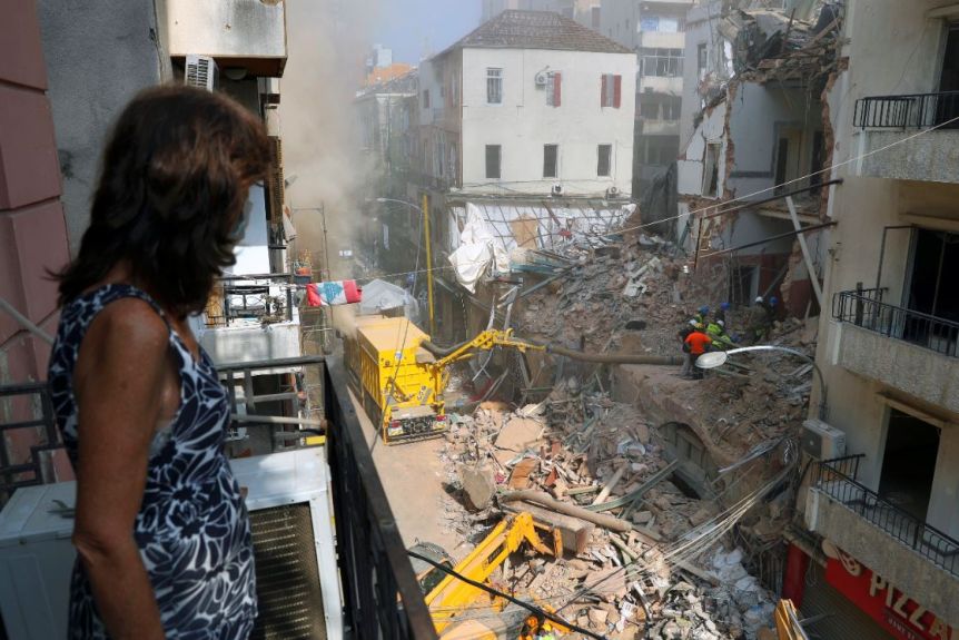 A woman stands on her balcony as she looks at rescuers searching the site of a collapsed building in Beirut