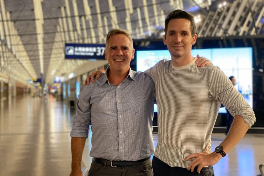 Smith and Bertels hold their arms around each other's shoulders as they stand in the middle of the terminal at Shanghai Airport.