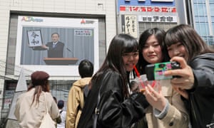 Young women take selfies as the big screen of Yoshihide Suga's broadcast