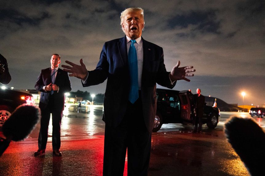 President Donald Trump speaks to reporters as he stands on the tarmac at night.