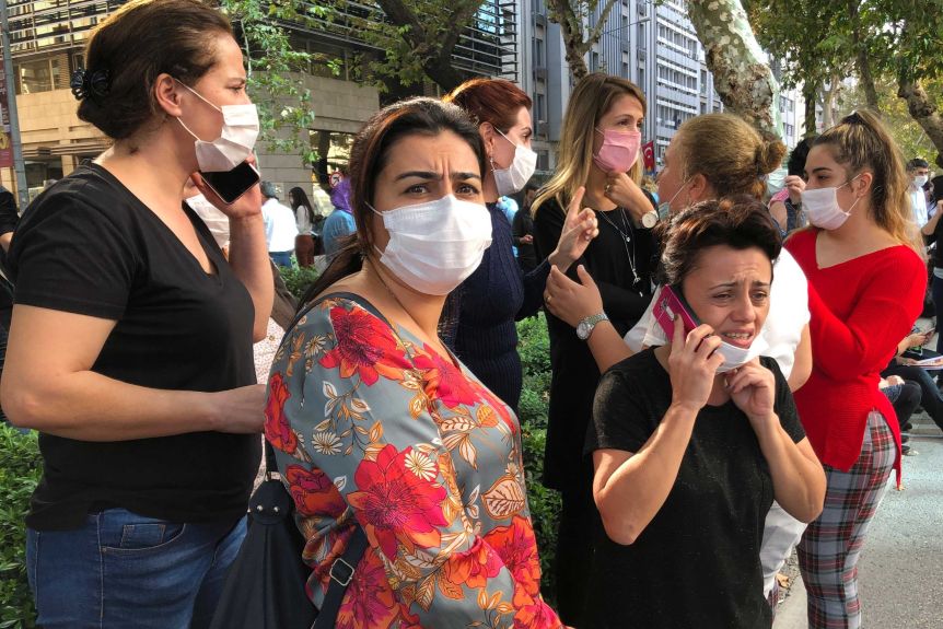 A group of women wearing masks are standing on their faces in the street, some of them talking on their phones