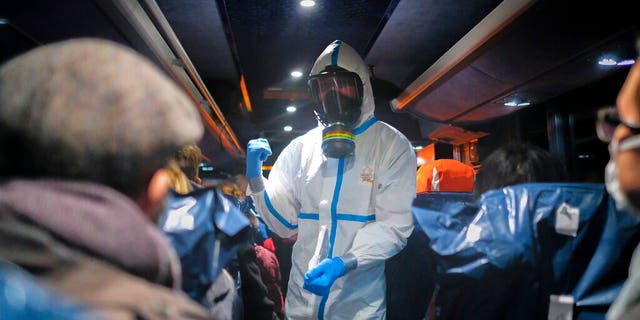 A military officer in a protective suit gives instructions to evacuees from Wuhan, China, as they travel to hospital after arriving at a military base in Wroclaw, Poland.  (AP Photo/ Arek Rataj, File)